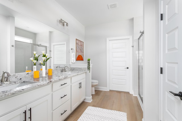 bathroom with a shower stall, wood finished floors, double vanity, toilet, and baseboards