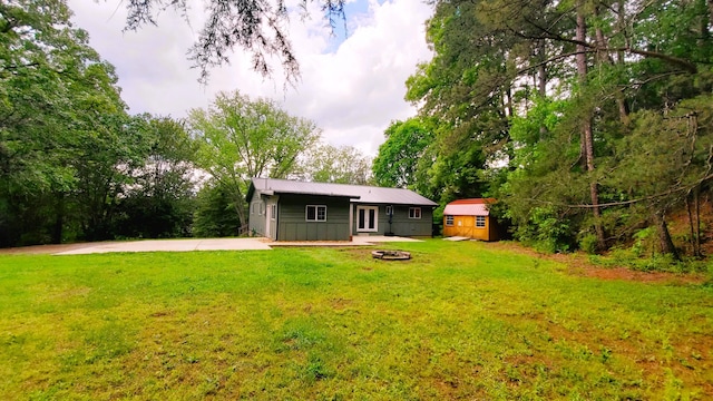 rear view of property featuring a storage unit, an outdoor fire pit, a yard, and an outbuilding