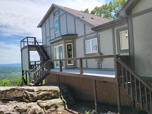 rear view of house with a deck, a shingled roof, stairs, and stucco siding