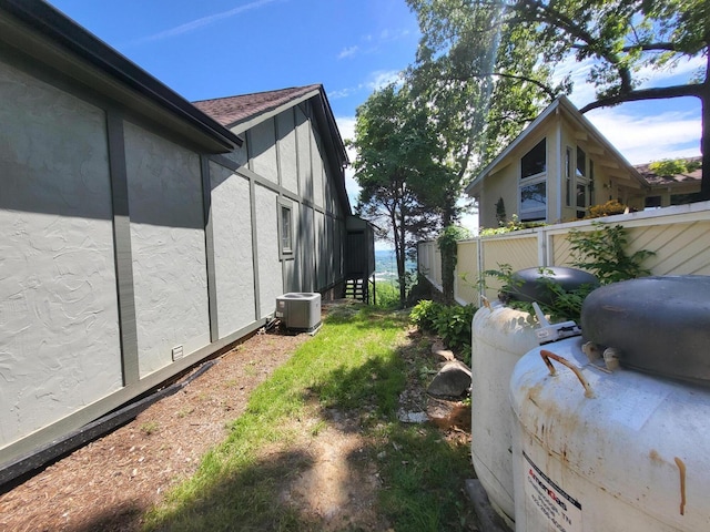 view of side of property with fence, stucco siding, and cooling unit