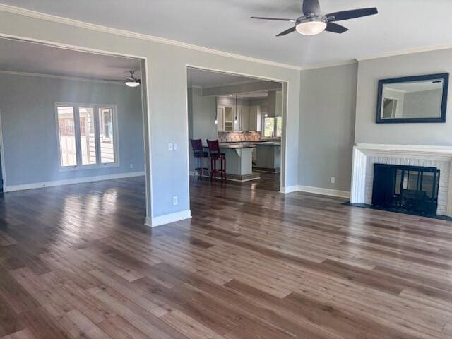 unfurnished living room with baseboards, ornamental molding, ceiling fan, and dark wood-style floors