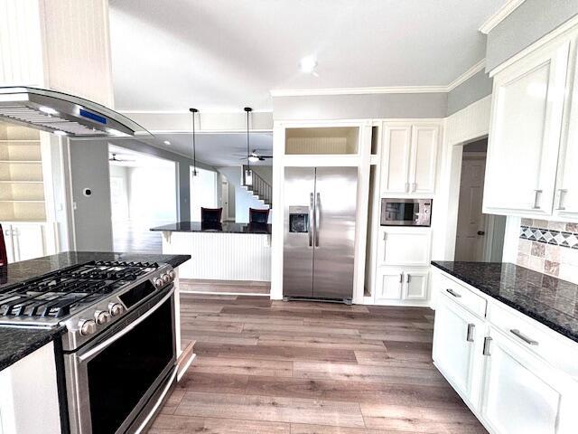 kitchen with crown molding, extractor fan, stainless steel appliances, white cabinetry, and decorative backsplash