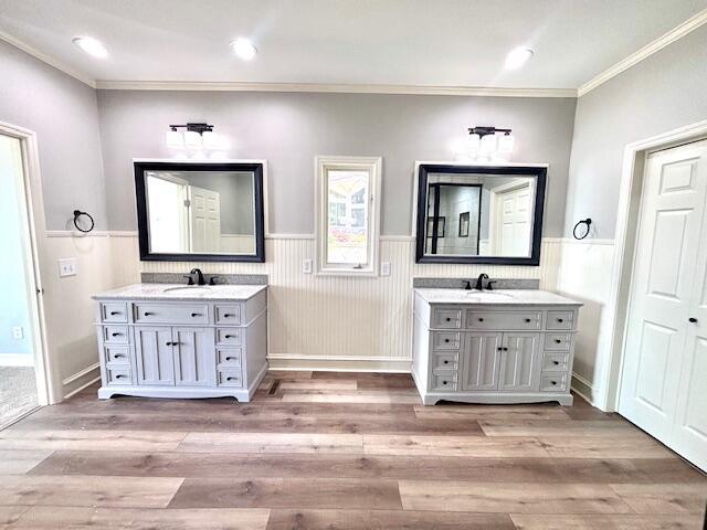 bathroom featuring ornamental molding, a sink, a wainscoted wall, and two vanities