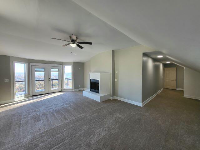 unfurnished living room with baseboards, ceiling fan, a fireplace with raised hearth, carpet, and vaulted ceiling