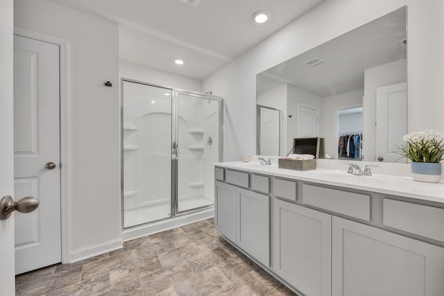 full bath featuring double vanity, a walk in closet, a shower stall, and a sink