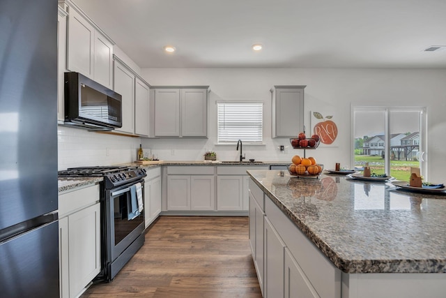 kitchen featuring backsplash, visible vents, appliances with stainless steel finishes, a sink, and stone counters