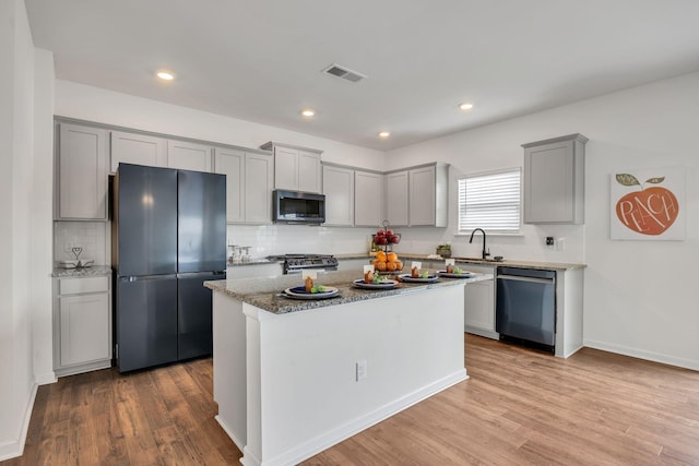 kitchen with decorative backsplash, wood finished floors, light stone counters, appliances with stainless steel finishes, and gray cabinetry