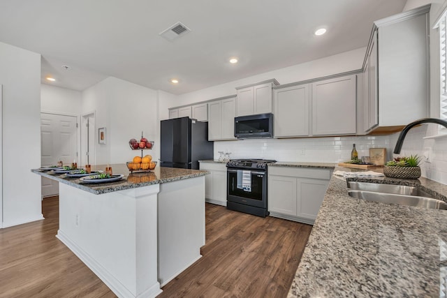 kitchen featuring dark wood-style flooring, a center island, a sink, backsplash, and black appliances