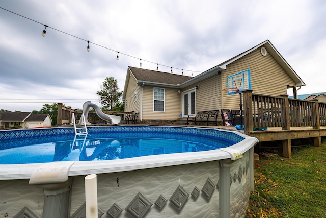 pool featuring a deck, a water slide, and french doors