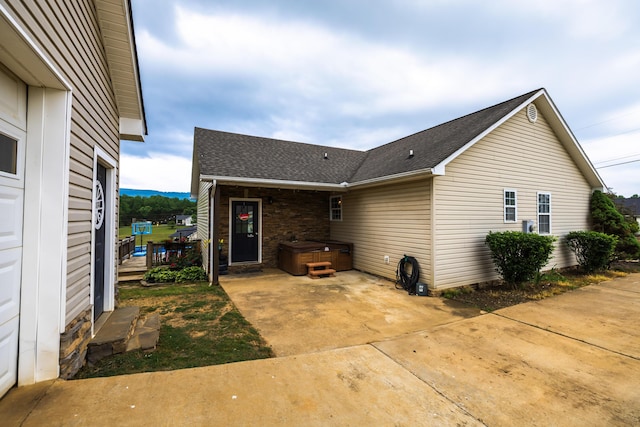 rear view of house featuring roof with shingles, a patio, a hot tub, and stone siding