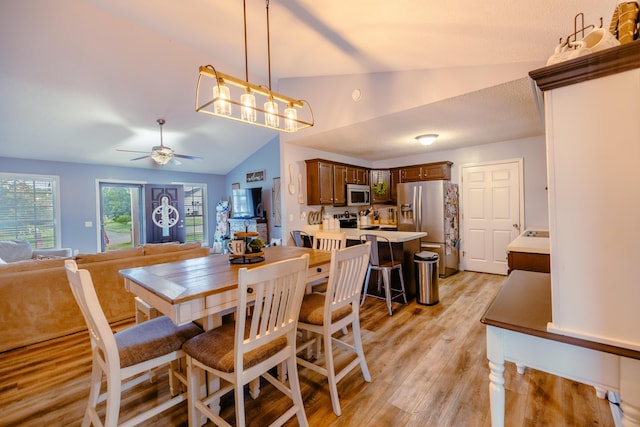 dining room with ceiling fan, vaulted ceiling, and light wood-type flooring
