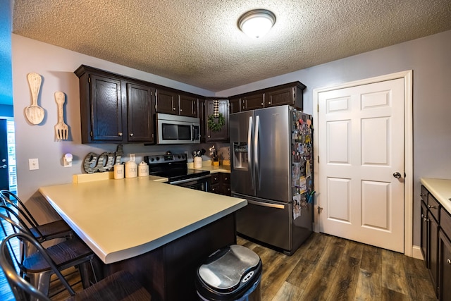 kitchen featuring appliances with stainless steel finishes, a breakfast bar, light countertops, a peninsula, and dark wood-style floors