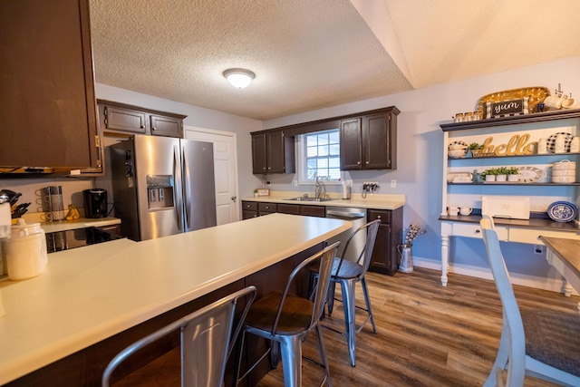 kitchen featuring a sink, light countertops, stainless steel appliances, a peninsula, and wood finished floors