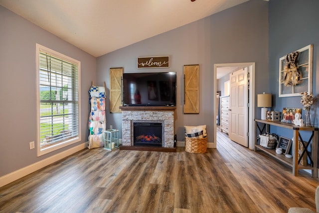 living area featuring baseboards, wood finished floors, a stone fireplace, and lofted ceiling