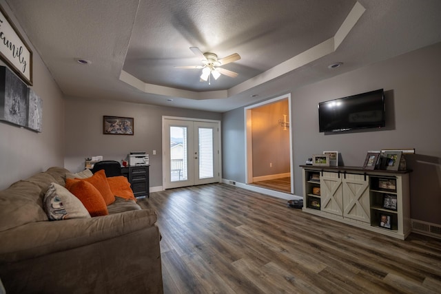 living area with french doors, a ceiling fan, a raised ceiling, baseboards, and dark wood-style floors