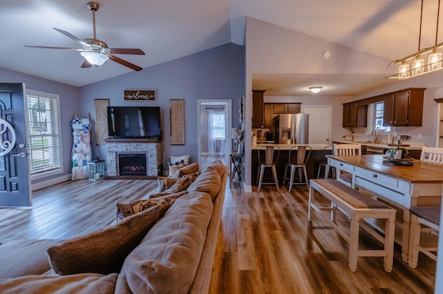 living area featuring a ceiling fan, a stone fireplace, wood finished floors, and lofted ceiling