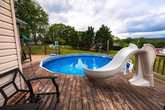 view of swimming pool with a wooden deck, a fenced in pool, a playground, a yard, and a water slide