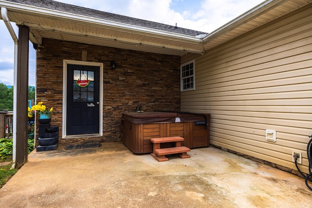 entrance to property featuring a shingled roof, a hot tub, and stone siding