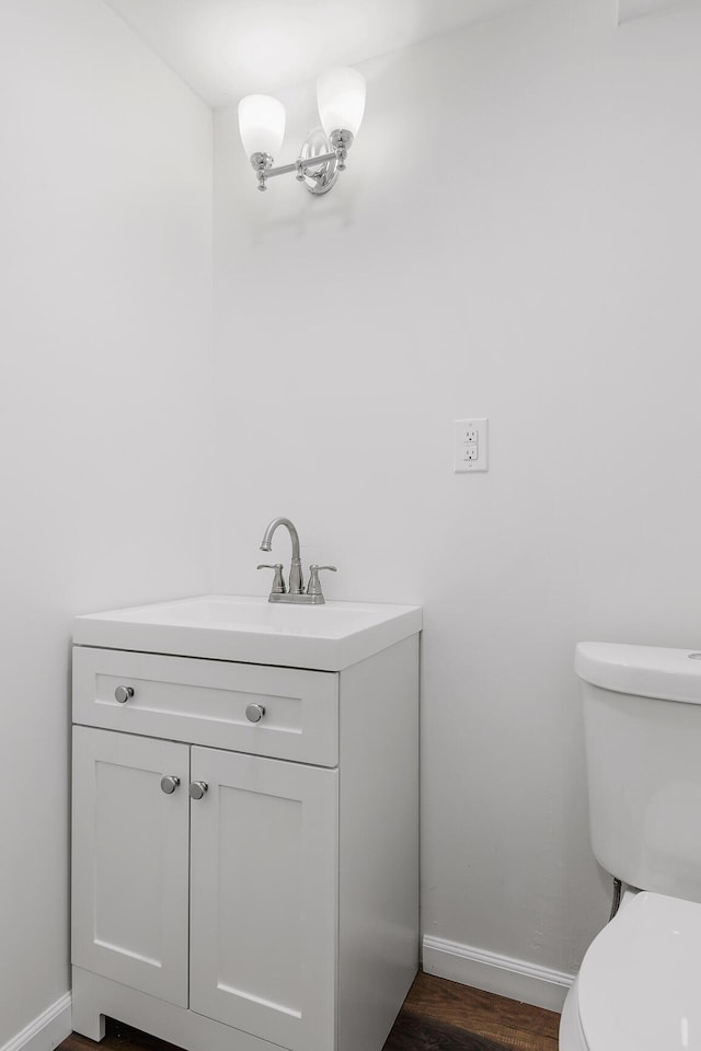 bathroom featuring toilet, baseboards, wood finished floors, and vanity