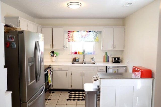 kitchen with appliances with stainless steel finishes, a sink, light tile patterned floors, white cabinets, and light countertops