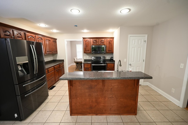 kitchen featuring dark countertops, a kitchen island with sink, stainless steel appliances, recessed lighting, and light tile patterned floors