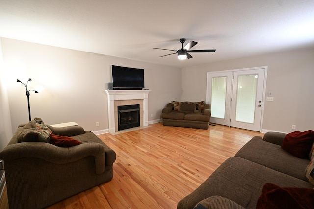 living area with a ceiling fan, baseboards, a tiled fireplace, and light wood-style flooring