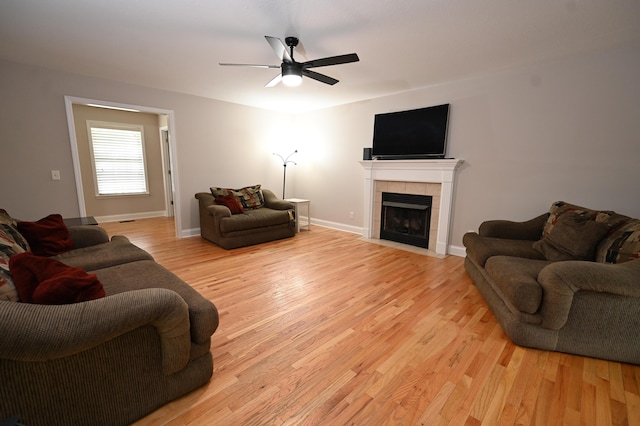 living room featuring a tiled fireplace, baseboards, a ceiling fan, and light wood finished floors