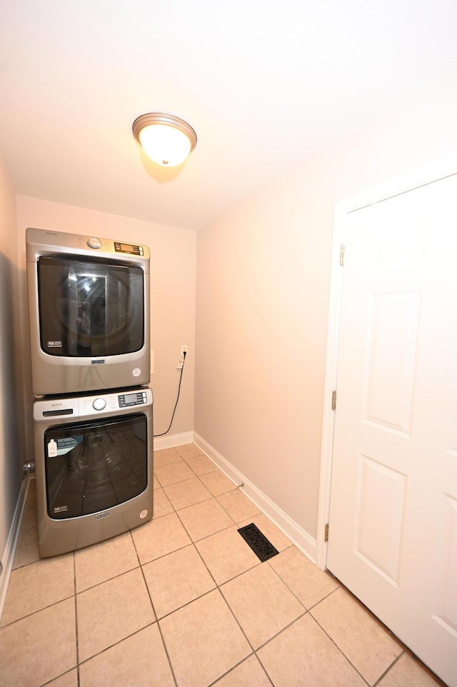 clothes washing area featuring laundry area, stacked washer and dryer, visible vents, light tile patterned floors, and baseboards