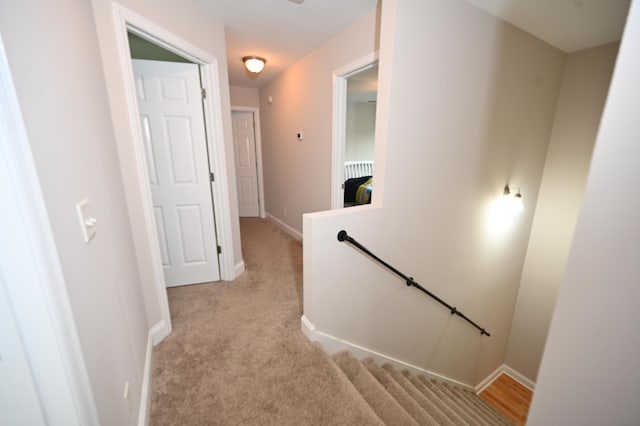 hall featuring baseboards, light carpet, and an upstairs landing