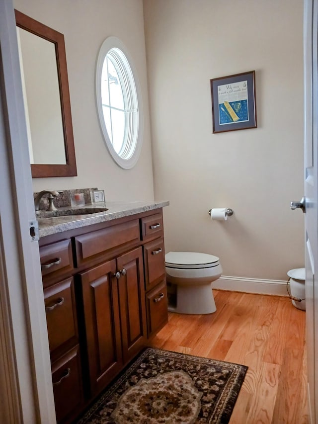 bathroom with toilet, baseboards, wood finished floors, and vanity