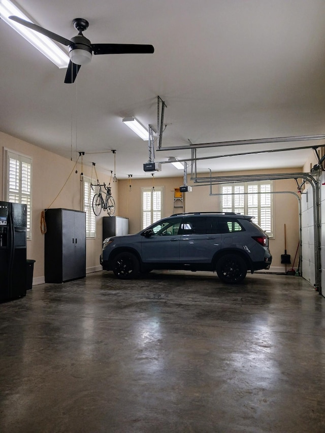 garage featuring baseboards, a garage door opener, a ceiling fan, and black refrigerator with ice dispenser