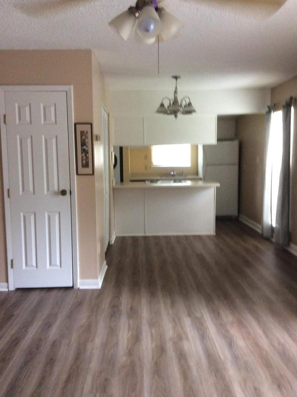 unfurnished living room featuring dark wood-type flooring, a textured ceiling, baseboards, and ceiling fan with notable chandelier