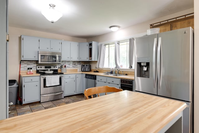 kitchen with decorative backsplash, light countertops, gray cabinets, a sink, and appliances with stainless steel finishes