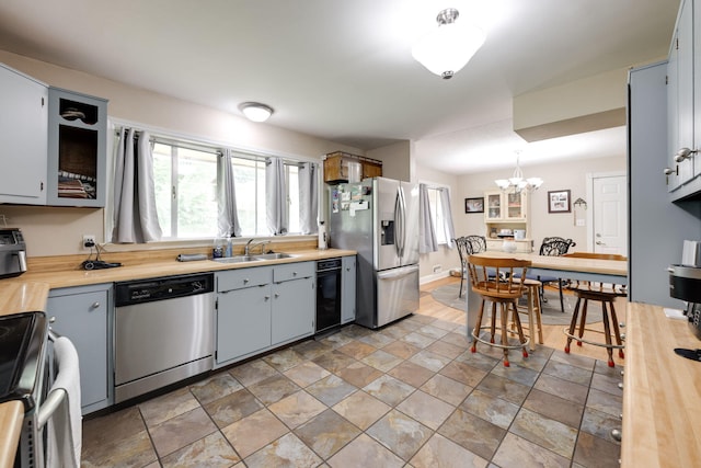 kitchen featuring a notable chandelier, appliances with stainless steel finishes, a sink, light countertops, and stone finish floor