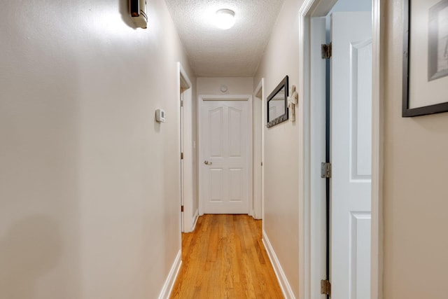 hallway featuring baseboards, light wood-type flooring, and a textured ceiling