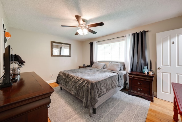 bedroom featuring a ceiling fan, a textured ceiling, baseboards, and light wood-style floors