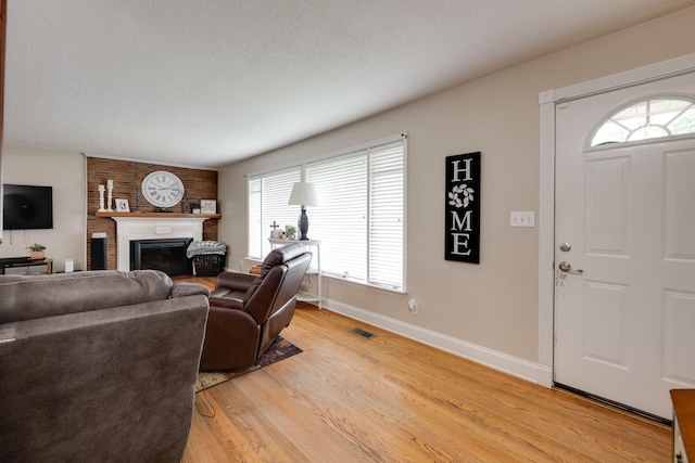 living room featuring a large fireplace, light wood-style flooring, baseboards, a healthy amount of sunlight, and visible vents