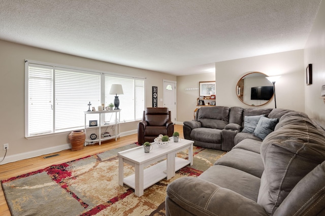 living area with baseboards, a textured ceiling, visible vents, and wood finished floors