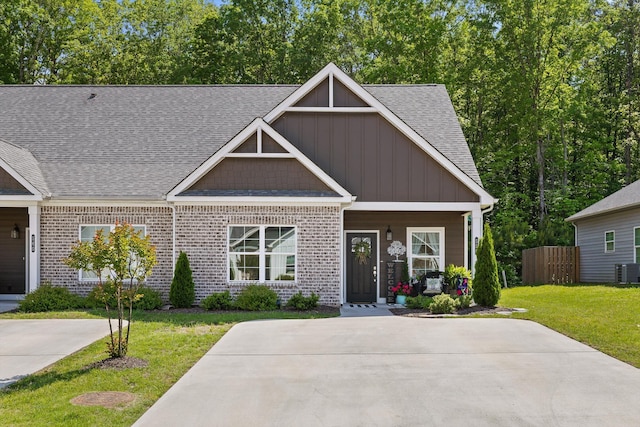 craftsman inspired home with board and batten siding, central air condition unit, brick siding, a front lawn, and a shingled roof