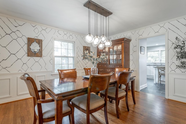 dining area with baseboards, crown molding, wallpapered walls, and wood finished floors