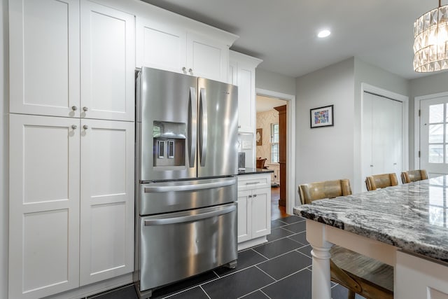kitchen featuring dark stone counters, dark tile patterned flooring, stainless steel fridge with ice dispenser, white cabinetry, and a chandelier