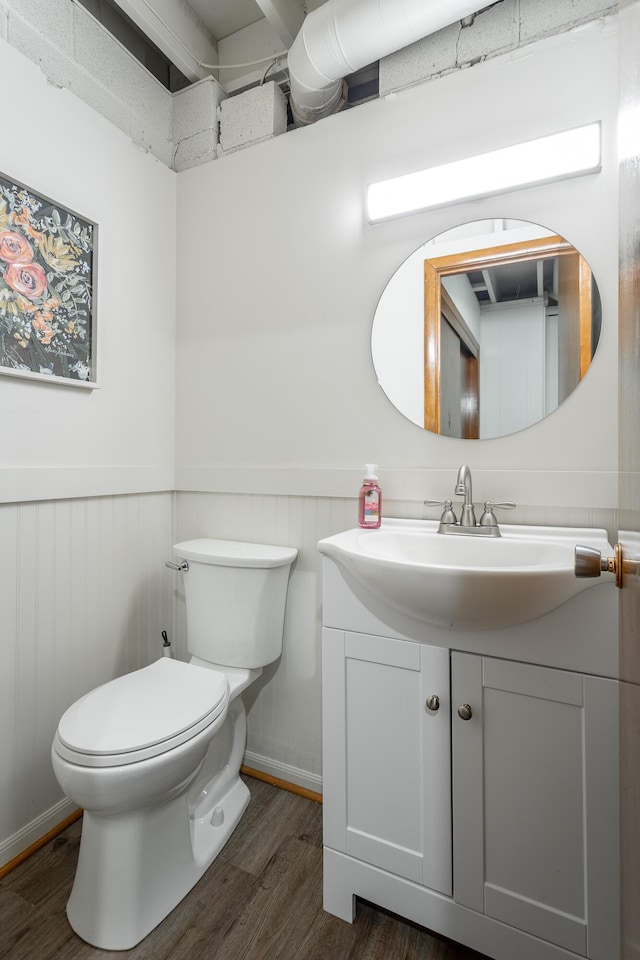 half bath featuring toilet, wainscoting, wood finished floors, and vanity