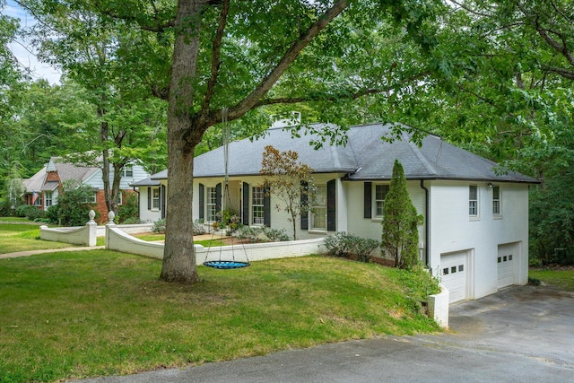 ranch-style house featuring a front yard, an attached garage, a shingled roof, and driveway