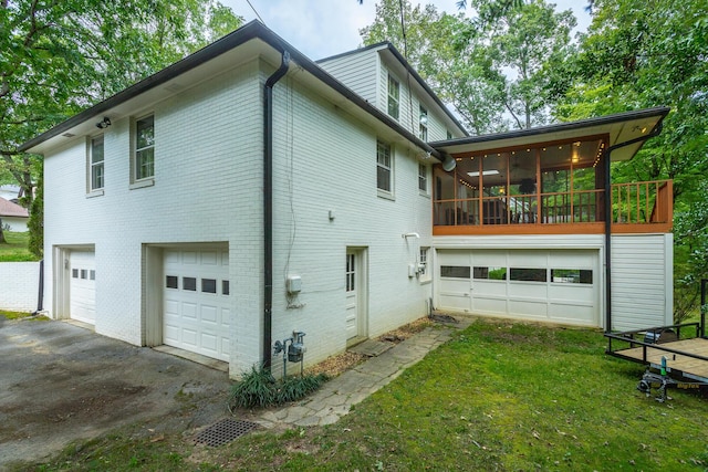 back of house with a garage, a sunroom, a yard, aphalt driveway, and brick siding