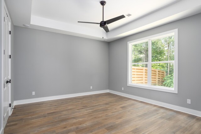 empty room featuring baseboards, a raised ceiling, ceiling fan, and wood finished floors