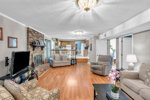 living area featuring crown molding, a brick fireplace, light wood-type flooring, and a textured ceiling