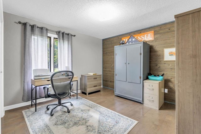 office space featuring light wood-style floors, wood walls, a textured ceiling, and baseboards