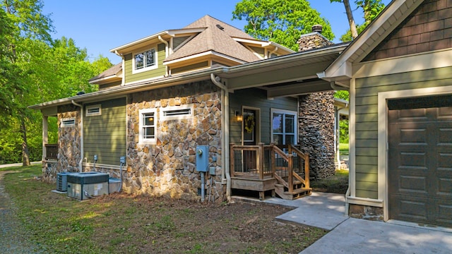 view of property exterior featuring central AC, a chimney, a shingled roof, and stone siding