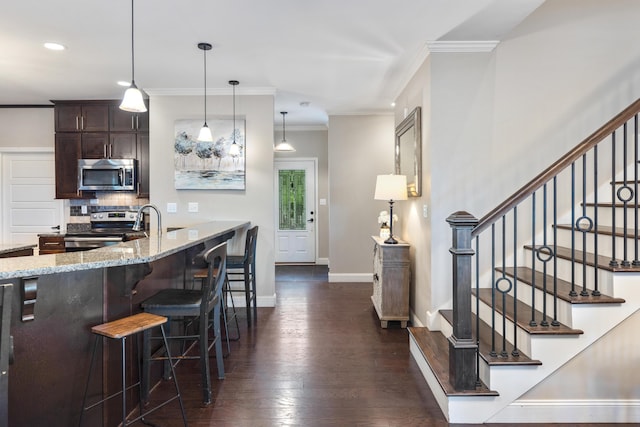 kitchen with dark brown cabinets, a breakfast bar, light stone counters, stainless steel appliances, and dark wood-style floors