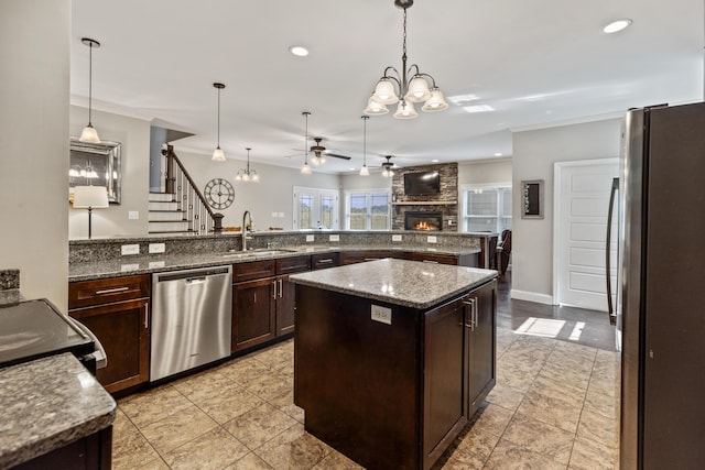 kitchen featuring appliances with stainless steel finishes, a large fireplace, dark brown cabinets, a sink, and ceiling fan with notable chandelier